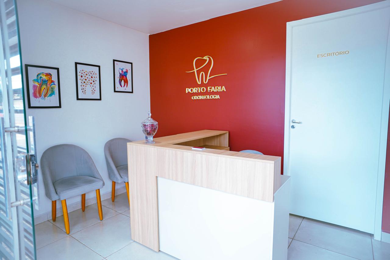 Recepção da Porto Faria Odontologia: parede marsala com o logotipo da clínica em dourado, balcão de atendimento em madeira clara e poltronas bege